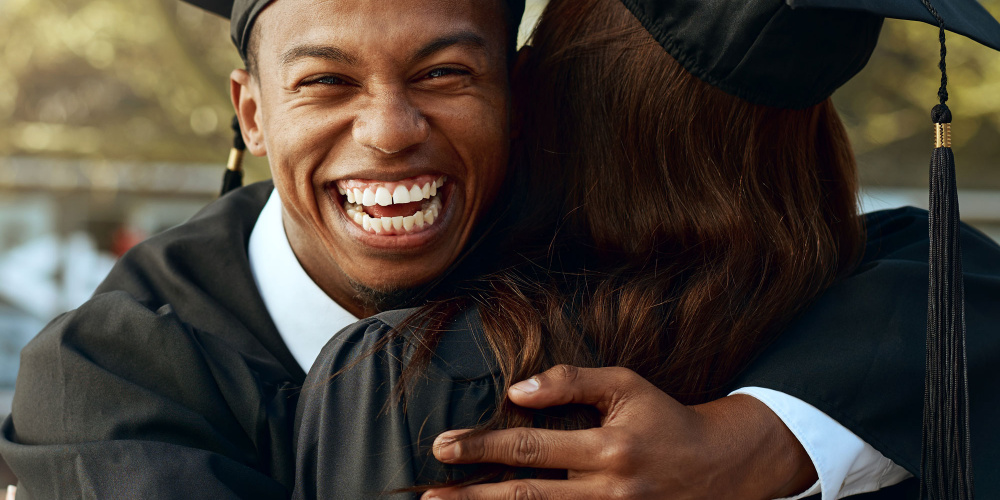 Portrait of a happy young man and woman hugging on graduation day.
