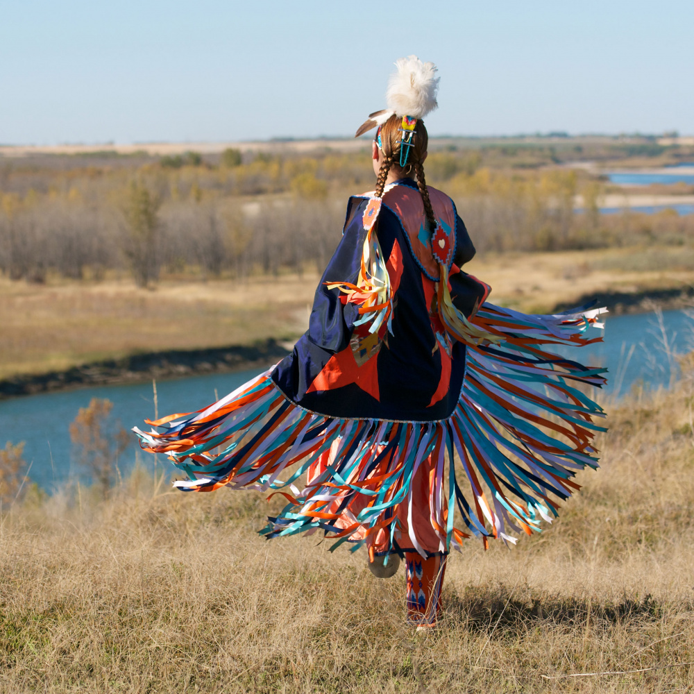 Indigenous woman dancing is colorful shaw on top of hill overlooking river